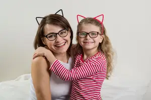 Smiling mother and daughter wearing eyeglasses with cat ear headbands.